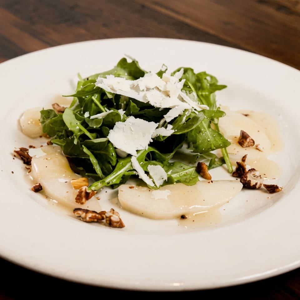 Arugula salad with shaved cheese, sliced fruit, toasted nuts, and light dressing on a white plate atop a wooden table.